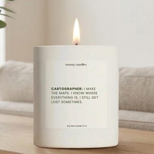 May include: A lit white soy wax candle with the text "sunny candles" and a quote about cartographers. The candle is 9 oz and sits on a wooden surface.