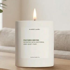 May include: A lit white soy wax candle with the text "FEATURES WRITER: SCENTED WITH EDITORIAL AND QUIET FURY." The candle is 9 oz and sits on a wooden surface. The brand name "wenfield candles" is also visible.