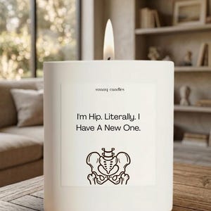 May include: A white candle with a lit wick. The candle has a label that reads "I'm Hip. Literally. I Have A New One." with a graphic of a pelvis. The brand name "sunny candles" is also on the label.