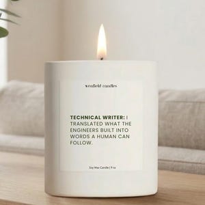 May include: A lit white soy wax candle with the text "TECHNICAL WRITER: I TRANSLATED WHAT THE ENGINEERS BUILT INTO WORDS A HUMAN CAN FOLLOW." The candle is 9 oz and sits on a wooden surface.
