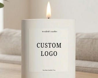 May include: A white cylindrical soy wax candle with a lit flame. The label features the text wenfield candles, CUSTOM LOGO, and Soy Wax Candle | 9 oz. The candle is housed in a smooth matte white container, providing a clean and simple aesthetic.