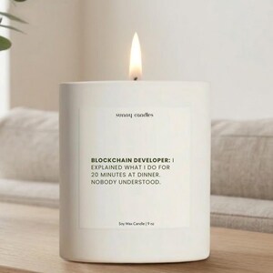 May include: A lit white soy wax candle with the text "BLOCKCHAIN DEVELOPER: I EXPLAINED WHAT I DO FOR 20 MINUTES AT DINNER. NOBODY UNDERSTOOD." The candle is 9 oz and has the brand name "sunny candles".