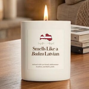 May include: A white cylindrical candle with a lit wick. The label features a map of Latvia filled with the national flag colors, the text "Smells Like a Badass Latvian," and "Infused with rye bread, midsummer bonfires, and Baltic pride."