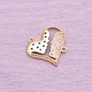 May include: A gold-toned heart-shaped jewelry charm featuring a split design. One side is inlaid with small, dark blue circular stones, while the other side is encrusted with numerous clear, sparkling white crystals. Two small loops are attached.