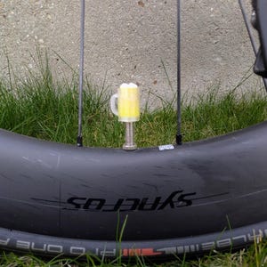 May include: A bicycle wheel with a yellow beer-shaped valve cap. The wheel is black with the word "SYNEROS" printed on the side. The background is green grass.