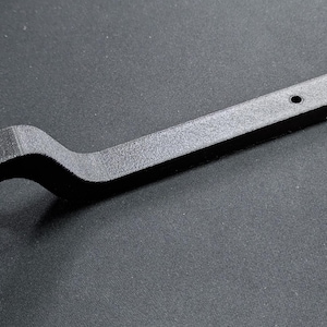 May include: A black bottle opener with a unique design. The opener has a curved handle with two holes and a circular opening with two smaller holes. The opener is approximately 7 inches long.