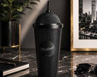 May include: A matte black studded tumbler with a matching lid and straw. The exterior features a circular black emblem in the center with the name Michael printed in a white script font, followed by the text APRIL 2024 in a smaller sans-serif font.