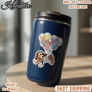 May include: A dark blue insulated tumbler with a black lid featuring a sticker of a brown dachshund with a spring-like body holding a cluster of colorful Mickey Mouse-shaped balloons. The sticker depicts the dog with long ears and a tan face.