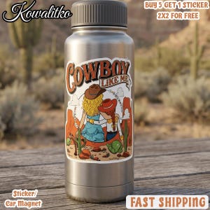 Op de afbeelding: Een zilverkleurige metalen waterfles met een sticker met de tekst Cowboy Like Me. De sticker toont twee figuren met blond en rood haar die cowboyhoeden dragen, staand in een woestijnlandschap met cactussen en rotsformaties.