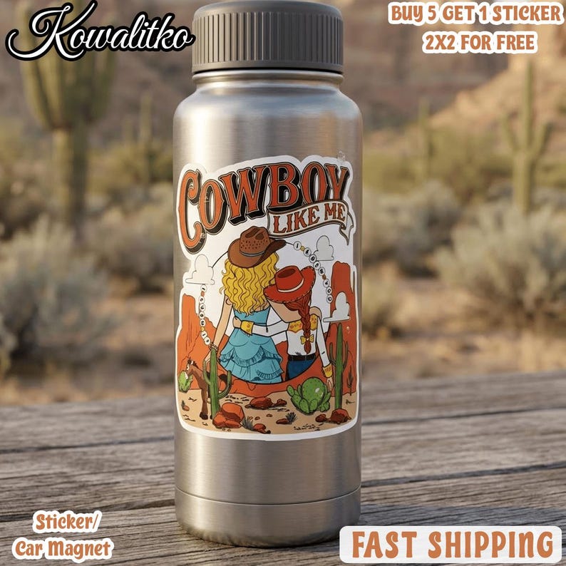 Op de afbeelding: Een zilverkleurige metalen waterfles met een sticker met de tekst Cowboy Like Me. De sticker toont twee figuren met blond en rood haar die cowboyhoeden dragen, staand in een woestijnlandschap met cactussen en rotsformaties.