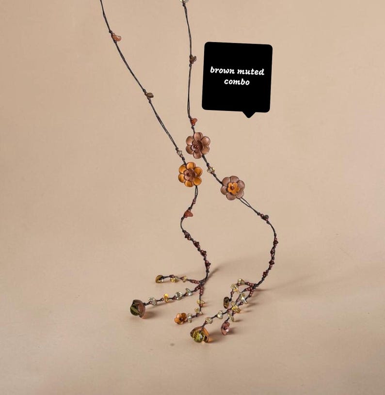 May include: A long, delicate necklace featuring thin dark brown cord strands adorned with small, metallic-toned flower charms and scattered beads in earthy hues. A black speech bubble graphic contains the white text brown muted combo.