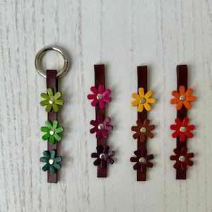 May include: Five leather keychains with a silver ring. Each keychain has five colorful flower charms in shades of green, pink, orange, and yellow.