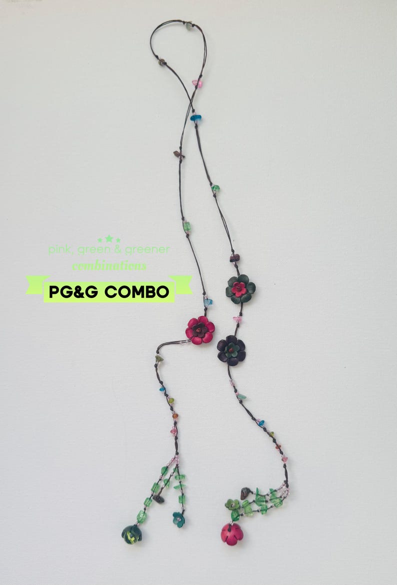 May include: A long necklace on a thin dark cord featuring scattered small colorful beads and several carved flower-shaped charms in shades of pink, green, and dark gray. The text "pink, green & greener combinations" and "PG&G COMBO" is visible.