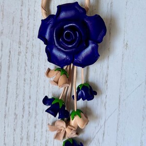 May include: A leather rose keychain with a blue rose and smaller blue and beige flowers hanging from it.