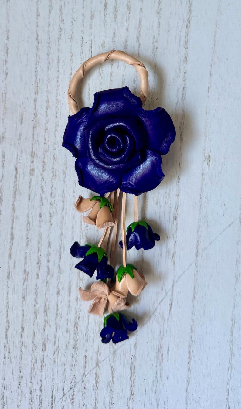 May include: A leather rose keychain with a blue rose and smaller blue and beige flowers hanging from it.