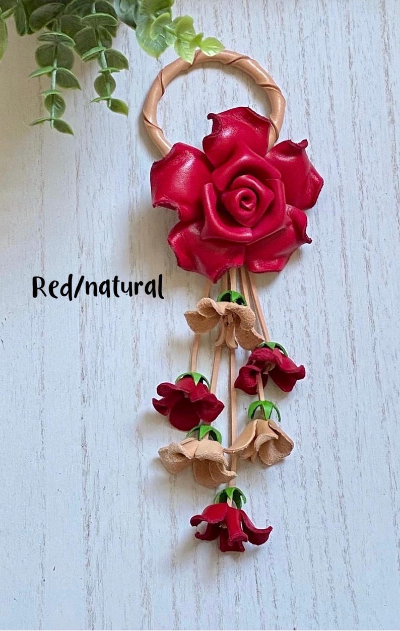 May include: A leather keychain with a red rose and a dangling chain of red and beige flowers. The text "Red/natural" is visible in the image.