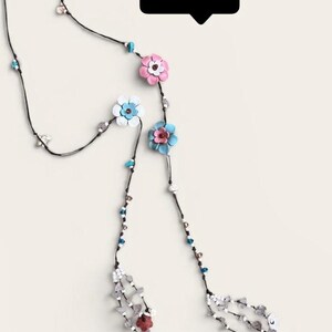 May include: A long necklace featuring a thin black cord adorned with small colorful beads and several layered leather-style flower charms in shades of pink, blue, and white. The ends feature dangling bead clusters and a black speech bubble with the text pastel pwb.
