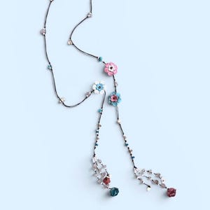 May include: A long lariat-style necklace featuring a thin black cord adorned with small turquoise, clear, and metallic beads. The necklace includes several multi-colored flower charms in shades of pink, white, light blue, and dark red, ending in tassels.