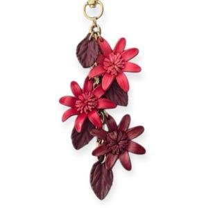 K&ouml;nnte beinhalten: Ein Schl&uuml;sselanh&auml;nger mit floralem Thema mit drei roten Blumenanh&auml;ngern mit detaillierten Bl&uuml;tenbl&auml;ttern und dunkelroten Bl&auml;ttern. Die Blumen sind durch eine goldene Kette verbunden und an einem goldfarbenen Verschluss befestigt.