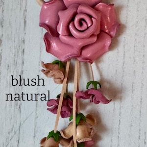 May include: A leather rose keychain with a blush pink rose and smaller pink and beige flowers hanging from a tan leather loop.