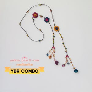 May include: A long necklace featuring a dark cord adorned with small multi-colored beads and several flower-shaped charms in shades of yellow, blue, and rose. The text on the image reads: yellow, blue & rose combination YBR COMBO.