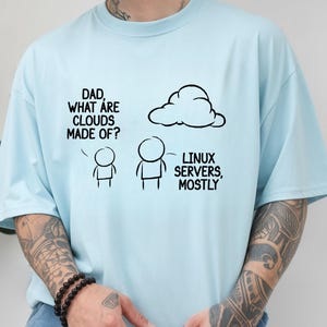 May include: Light blue t-shirt with a humorous graphic. The graphic features stick figures and a cloud, with the text "DAD, WHAT ARE CLOUDS MADE OF?" and "LINUX SERVERS, MOSTLY". The shirt is a casual wear item.