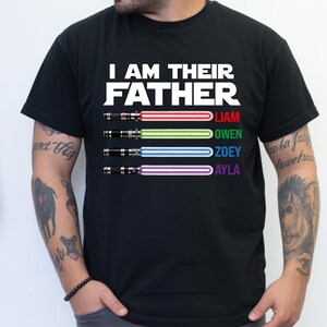 Pu&ograve; includere: T-shirt nera con la scritta bianca "I AM THEIR FATHER". Sotto, quattro spade laser rosse, verdi, blu e viola, con i nomi Liam, Owen, Zoey e Ayla. Design a tema Star Wars.