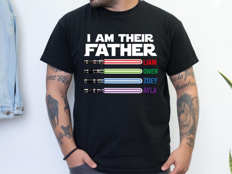 Pu&ograve; includere: T-shirt nera con la scritta bianca "I AM THEIR FATHER". Sotto, quattro spade laser rosse, verdi, blu e viola, con i nomi Liam, Owen, Zoey e Ayla. Design a tema Star Wars.