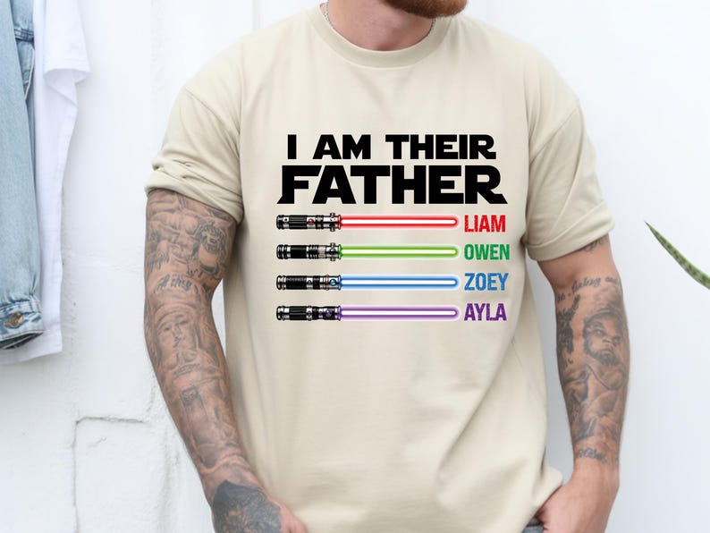 Pu&ograve; includere: T-shirt beige con la scritta nera "I AM THEIR FATHER". Sotto, quattro spade laser con i nomi Liam, Owen, Zoey e Ayla in rosso, verde, blu e viola.