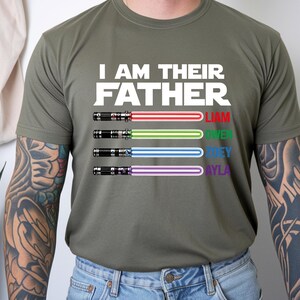 Pu&ograve; includere: T-shirt verde oliva con la scritta bianca "I AM THEIR FATHER". Sotto, quattro spade laser con i nomi Liam, Owen, Joey e Ayla in diversi colori. Le spade laser hanno lame rosse, verdi, blu e viola.