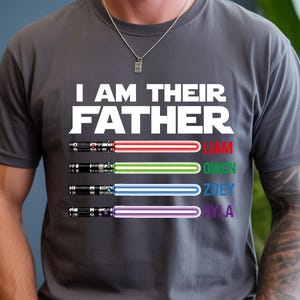Pu&ograve; includere: T-shirt grigia con la scritta bianca "I AM THEIR FATHER". Sotto, quattro spade laser rosse, verdi, blu e viola, con i nomi Liam, Owen, Zoey e Ayla. La maglietta &egrave; girocollo.