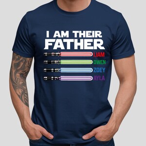Pu&ograve; includere: T-shirt blu navy con la scritta bianca "I AM THEIR FATHER". Sotto, quattro spade laser colorate con i nomi Liam, Owen, Zoey e Ayla. La maglietta &egrave; a girocollo.