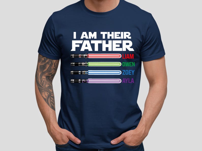 Pu&ograve; includere: T-shirt blu navy con la scritta bianca "I AM THEIR FATHER". Sotto, quattro spade laser colorate con i nomi Liam, Owen, Zoey e Ayla. La maglietta &egrave; a girocollo.