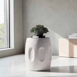 May include: A speckled white concrete plant stand with three oval cutouts. A small potted plant with green leaves sits on top. The stand is near a window and a neutral-toned wall. The stand is approximately 40 cm tall.