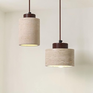 Puede incluir: Dos lámparas colgantes con pantallas cilíndricas beige texturizadas y tapas marrón oscuro. Las luces cuelgan de cables marrones sobre un fondo blanco. Las pantallas tienen un brillo cálido y acogedor.