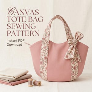 May include: A dusty pink canvas tote bag with floral patterned straps and a matching side bow. The text reads CANVAS TOTE BAG SEWING PATTERN Instant PDF Download. A stack of folded fabric and two wooden thread spools are visible below.