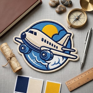 May include: Embroidered patch featuring a cream-colored airplane with blue accents, set against a blue sky with a yellow sun and clouds. The patch is surrounded by a cream-colored border. Other items include a compass, pen, notebook, and a rolled-up map.