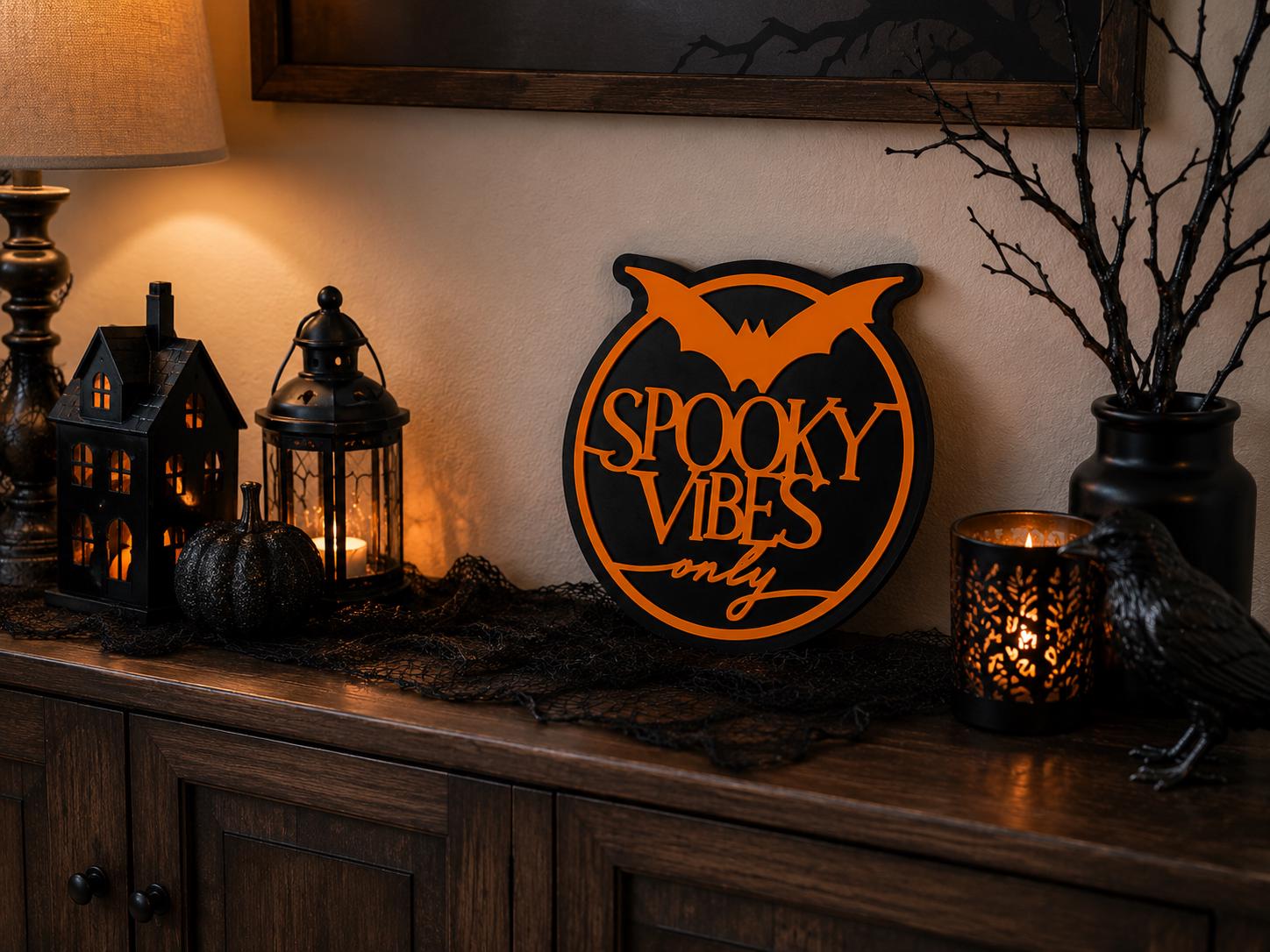 A circular sign saying Spooky Vibes Only with an orange bat, displayed on a wooden surface with Halloween decor.