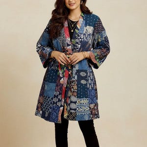 May include: A patchwork kimono-style jacket in shades of blue, red, and white. The jacket features a wrap-around design with a tie closure at the waist. The fabric appears to be quilted, with various patterns and textures. The sleeves are wide and three-quarter length.