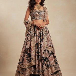 Könnte beinhalten: Eine Frau trägt ein traditionelles indisches Lehenga. Das Outfit besteht aus einem schwarzen Rock mit einem Blumenmuster in Rosa und Beige. Das Oberteil ist ein besticktes Crop-Top, und ein passender Schal ist über der Schulter drapiert. Das Ensemble ist elegant.
