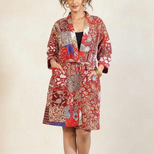 May include: A red patchwork robe with a paisley and floral pattern. The robe has a tie waist, pockets, and three-quarter sleeves. The robe is knee-length and features a mix of red, blue, and cream colors.