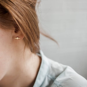 May include: A close-up of a person's ear with a small gold lightning bolt earring.