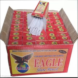 May include: A box of red and yellow "EAGLE" slate pencils. The box is open, revealing many individual red boxes of pencils and a bundle of white slate pencils. The box has text that reads "MADE FROM MANDSAUR'S BEST QUALITIES NATURAL STONE".