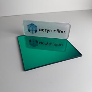 Peut inclure: Une plaque acrylique rectangulaire vert émeraude à la surface réfléchissante, placée sous une plaque signalétique rectangulaire transparente en acrylique avec un logo cube bleu et le texte noir "acrylonline" imprimé sur sa face avant.