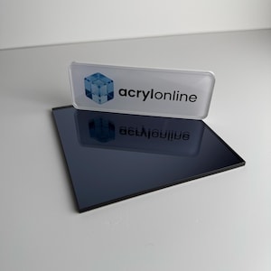 Peut inclure: Une plaque acrylique rectangulaire gris foncé et réfléchissante placée sous une plaque signalétique rectangulaire blanche. La plaque porte une icône de cube bleu en trois dimensions à gauche et le texte noir "acrylonline" à droite.