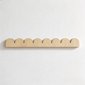 May include: A wooden wall shelf with a scalloped edge design. The shelf is made of light-colored wood and is mounted on a white wall. The shelf has a simple, modern aesthetic.