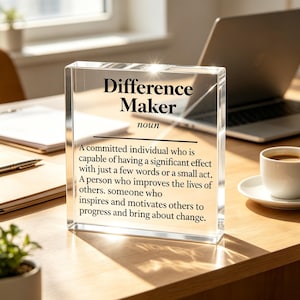 May include: A clear rectangular acrylic block desk sign featuring the black printed text: Difference Maker noun. A committed individual who is capable of having a significant effect with just a few words or a small act. A person who improves the lives of others. someone who inspires and motivates others to progress and bring about change.