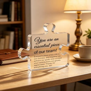 May include: A clear acrylic puzzle piece plaque featuring black printed text that reads: You are an essential piece of our team! Everyone plays a key role in our success, and together we achieve our goals and succeed. Your contributions are greatly appreciated. Thanks for everything you do!