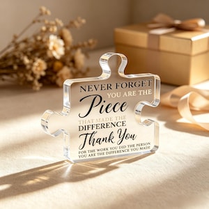 May include: A clear acrylic puzzle piece plaque featuring black printed text that reads: NEVER FORGET YOU ARE THE Piece THAT MADE THE DIFFERENCE Thank You FOR THE WORK YOU DID THE PERSON YOU ARE THE DIFFERENCE YOU MADE.