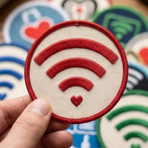 May include: A circular embroidered patch featuring a red Wi-Fi signal icon on a cream-colored background. The signal icon includes a small red heart at the base. The patch has a red stitched border and is part of a collection of similar patches.